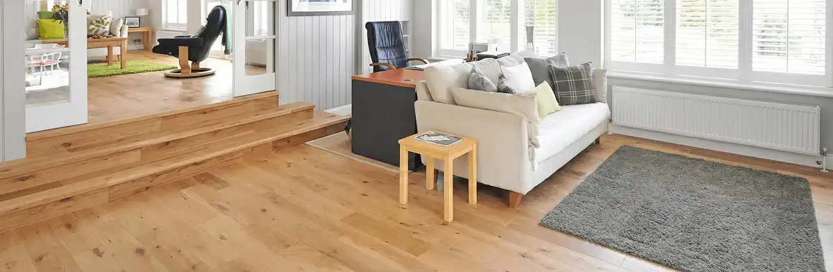 A modern living room with professionally installed laminate flooring, a beige sofa, a small side table, a gray rug, and large windows with white shutters in Duluth, MN